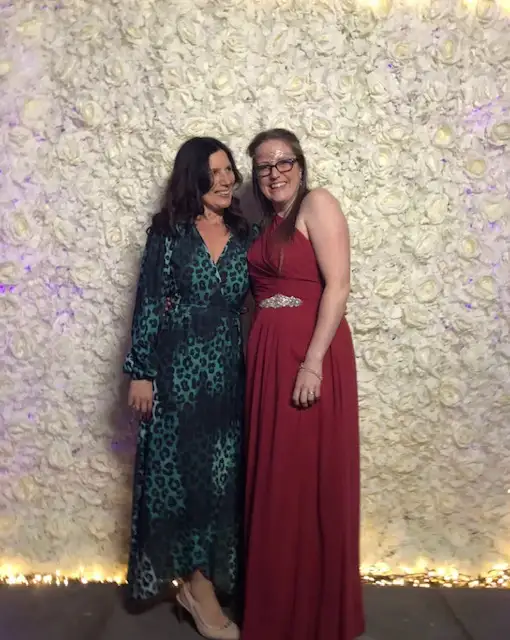Two guests posing in front of a white flower wall